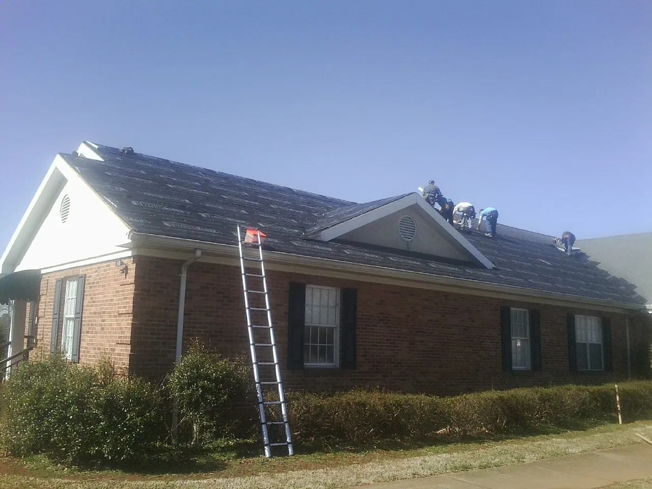 Crew tearing shingles off a brick ranch roof with a ladder set — Emergency Roof Repair work by our crew in Woods Hole
