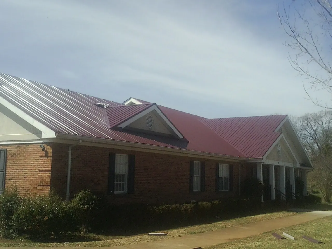Red metal roof with gabled entries on a long brick building, from a Hail Damage Roof Repair job in Woods Hole