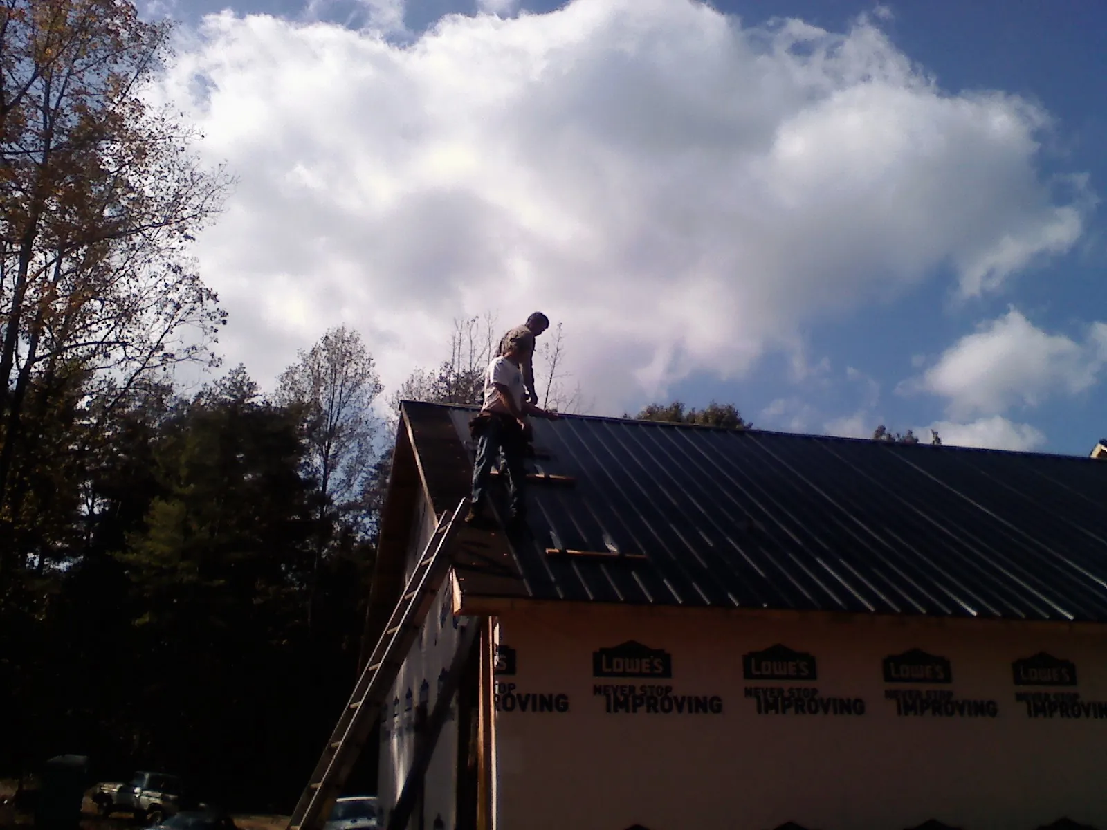 Roofer fastening dark metal panels high against a cloudy sky, from a Roof Inspection job in Woods Hole