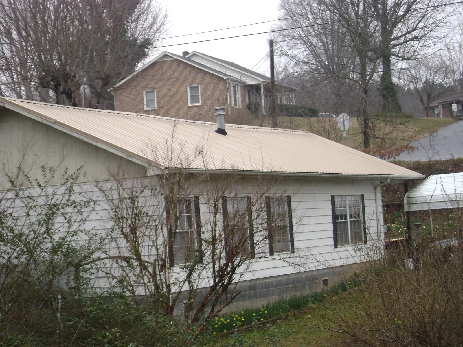 Tan metal roof on a white sided house set into a hillside — Commercial Roofing by Roofing Brothers in Woods Hole