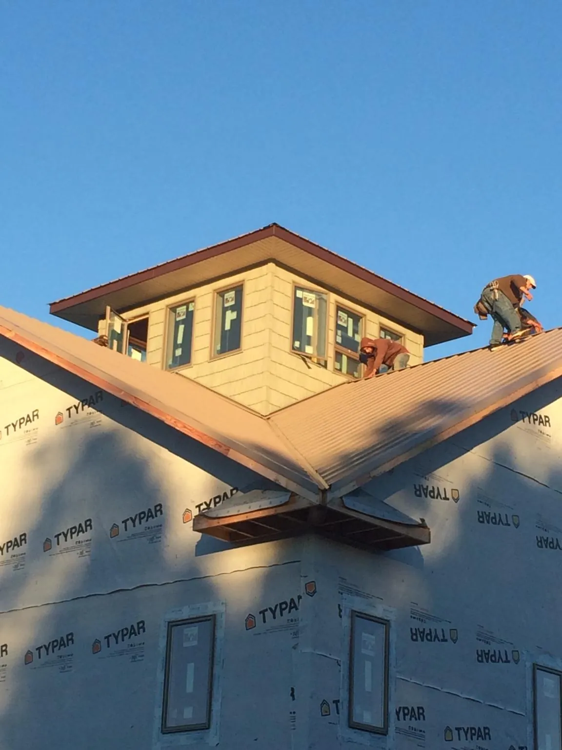 Roofers working around a rooftop cupola on a new metal roof at sunset — Roof Waterproofing in Woods Hole by Roofing Brothers